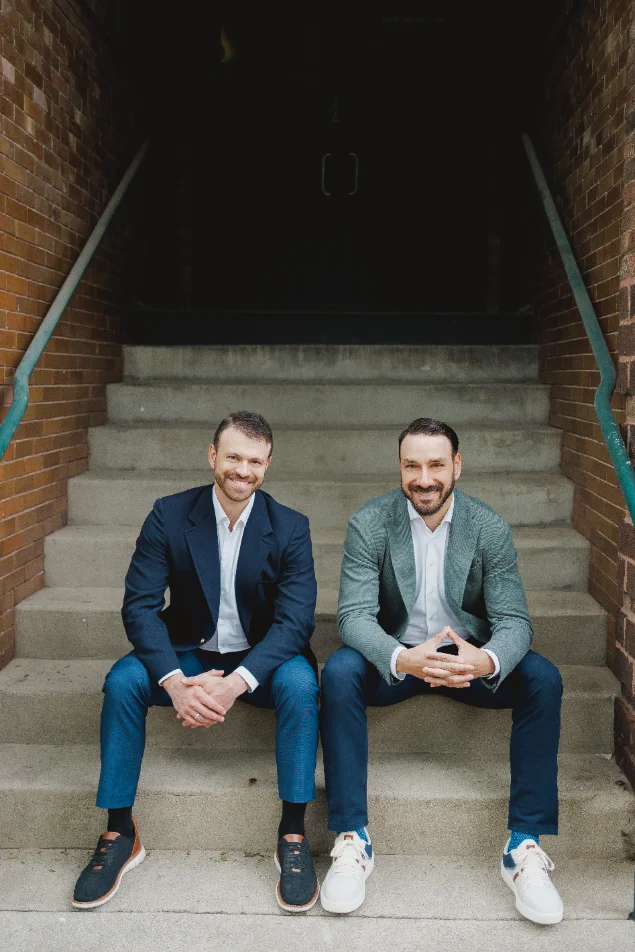 Lance daSilva and Mason Greenberg seated on brick building steps
